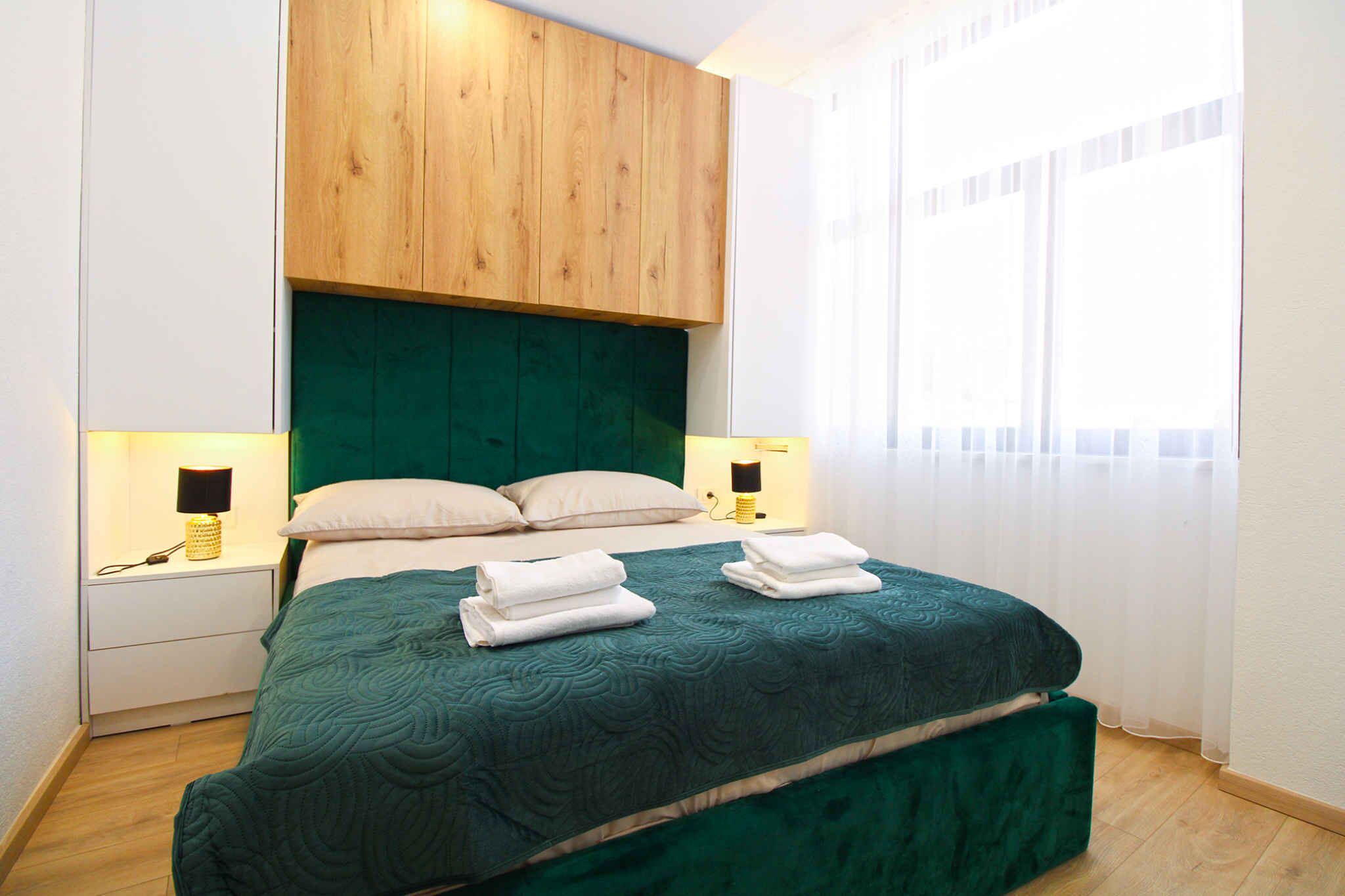 Een net opgemaakt bed met een groen hoofdeinde en twee bedlampjes.