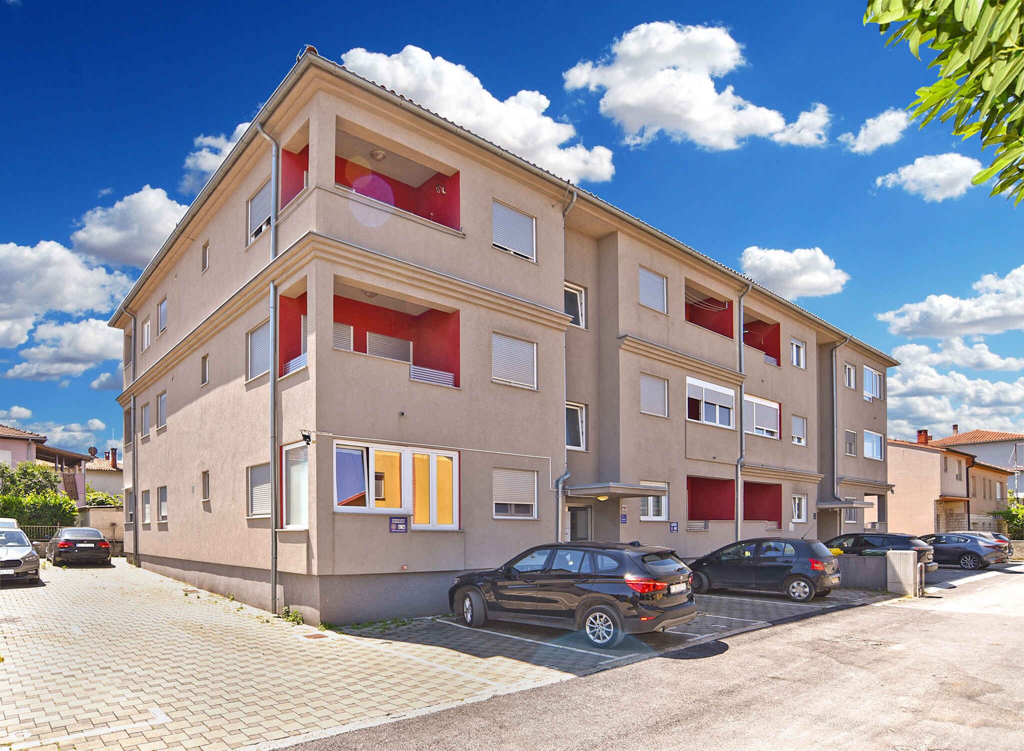 Ein mehrstöckiges Wohngebäude mit Balkonen, einem Parkplatz und wolkenlosem, blauem Himmel.
