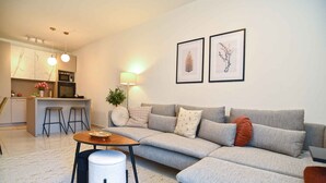 A modern living room with a grey sofa, a small round table, and a kitchen area in the background. - Holiday apartment with air conditioning (Pula)