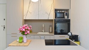 A modern kitchen with a marble backsplash, a built-in microwave, oven, and a central island with a sink and a vase of flowers. - Holiday apartment with air conditioning (Pula)