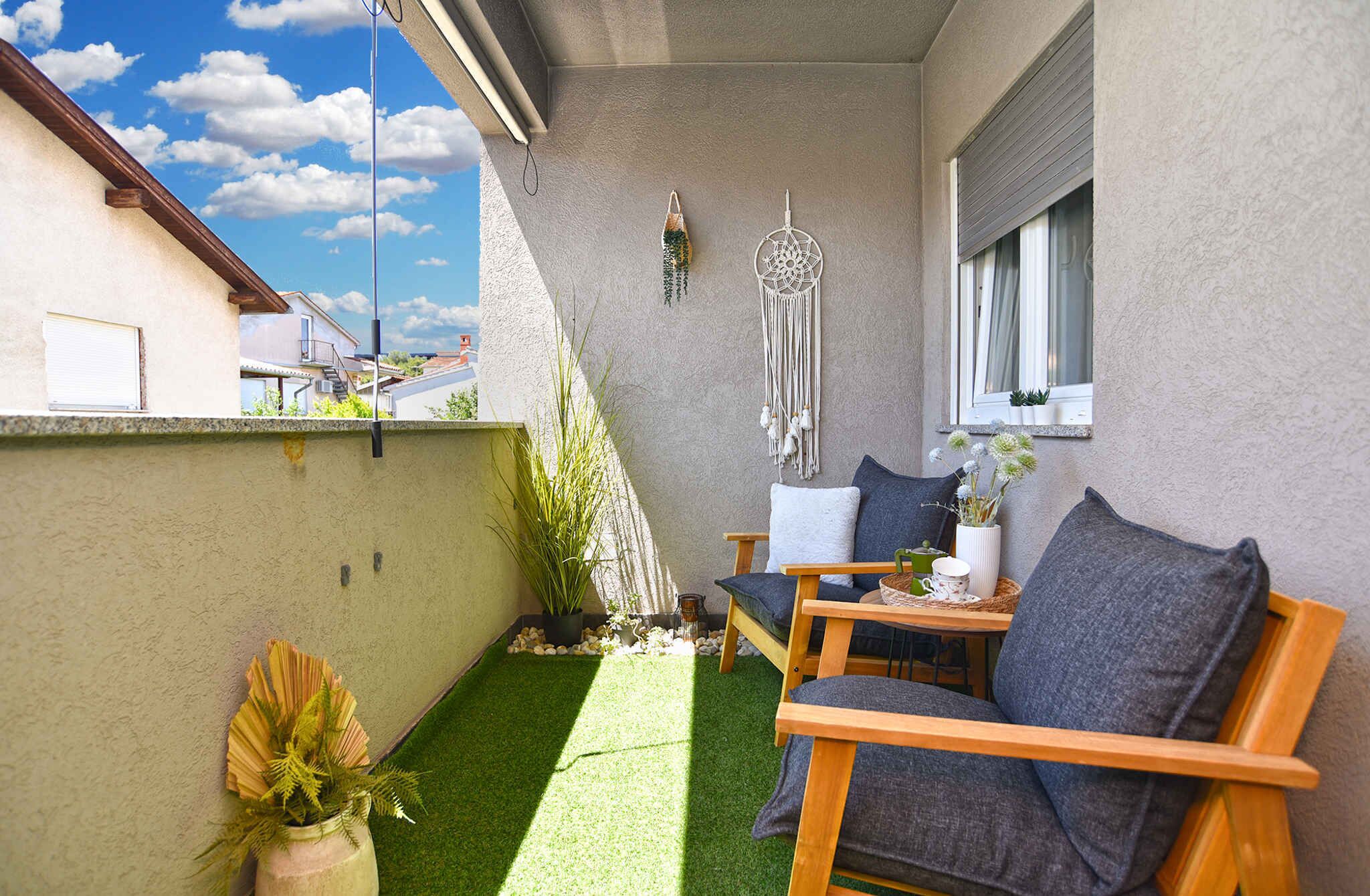 A small balcony with a wooden chair, a small table, and a decorative wall hanging.