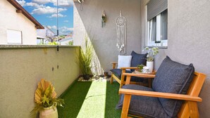 A small balcony with a wooden chair, a small table, and a decorative wall hanging. - Holiday apartment with air conditioning (Pula)