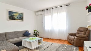 A living room with a grey sofa, a white coffee table, a brown armchair, and a painting on the wall. - Holiday apartment with air conditioning (Pula)