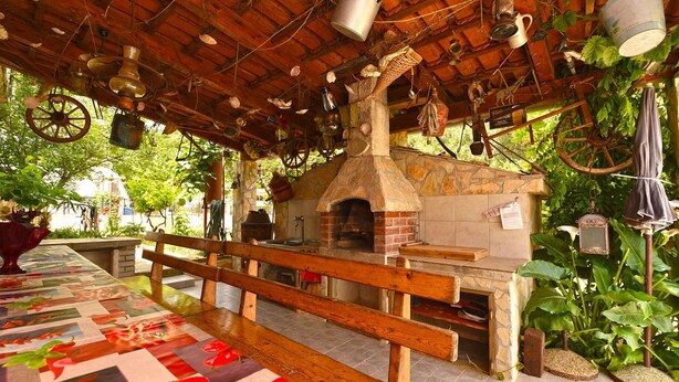 A rustic outdoor seating area with a stone fireplace, wooden benches, and hanging kitchen utensils. - Holiday apartment with air conditioning (Pula)