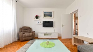 A living room with a sofa, a glass coffee table, a TV, and a painting on the wall. - Holiday apartment with air conditioning (Pula)