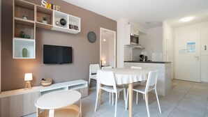 A modern kitchen with white cabinets, a built-in oven, and a dining area with a round table and white chairs.