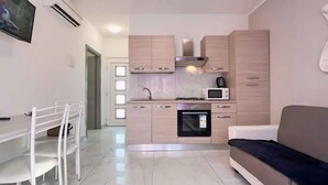 A modern kitchen with a built-in oven, microwave, and gas stove. There is a dining area with a white table and chairs, and a sofa in the living area.