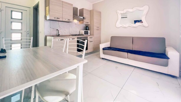 A modern kitchen with white cabinets, a dining table with chairs, a sofa, and a decorative mirror.