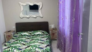 A bedroom with a bed, a mirror, a nightstand, a lamp, and a purple door.