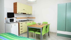 Une cuisine compacte équipée d’un four à micro-ondes, d’une cuisinière et de placards. On y trouve une table à manger avec des chaises, ainsi qu ’un lit recouvert d’une couverture à motifs.