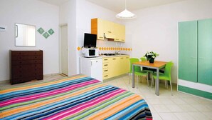 A bedroom with a colorful striped bedspread, a dresser, a small table with a plant, and a green chair. - Studio mit Klimaanlage (Bibione)