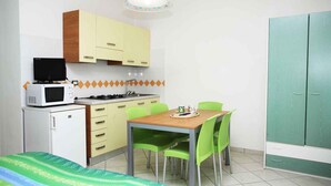 A compact kitchen with a microwave, stove, and sink. There is a dining table with chairs and a bed with a patterned blanket. - Studio mit Klimaanlage (Bibione)