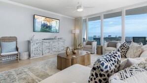 Ein geräumiges Wohnzimmer mit großem Fenster und Blick auf die Stadt, Deckenventilator und moderne Unterhaltungseinrichtung.