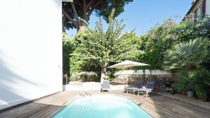 Une piscine avec une terrasse en bois, deux chaises longues, une table et un parasol.
