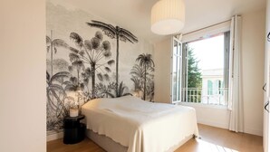 Une chambre à coucher comprenant un lit, une table de chevet, une fresque murale, une fenêtre avec vue et un luminaire suspendu.