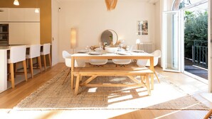 Un espace repas moderne avec une table en bois, des chaises blanches et un luminaire suspendu.