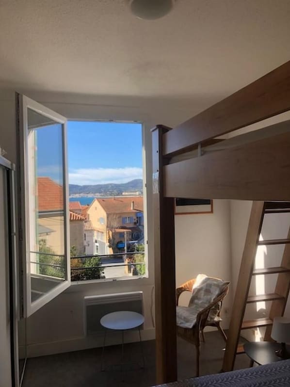 A room with a large window, a bunk bed, a small table, and a chair.