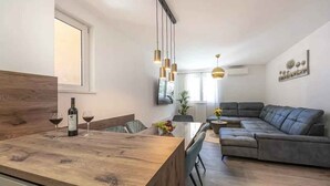 A modern living room with a wooden dining table, a grey sofa, and hanging pendant lights. - Holiday apartment with air conditioning and terrace (Crikvenica)