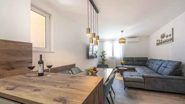 Un soggiorno moderno con un tavolo da pranzo in legno, un divano grigio e lampade a sospensione.