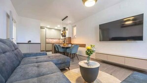 Un soggiorno moderno con un divano componibile, un tavolino rotondo con un vaso, una TV a schermo piatto montata a parete e un'area pranzo sullo sfondo.