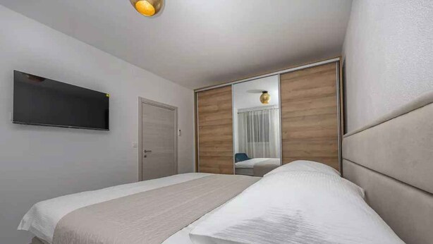 A modern hotel room with a large bed, a flat-screen TV mounted on the wall, and a sliding wooden wardrobe. - Holiday apartment with air conditioning and terrace (Crikvenica)