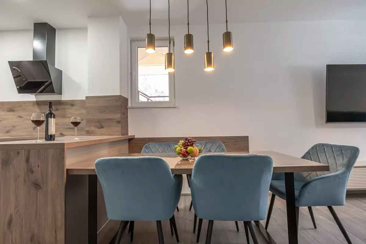 A modern dining area with a wooden table, four blue chairs, a fruit bowl, and pendant lights.