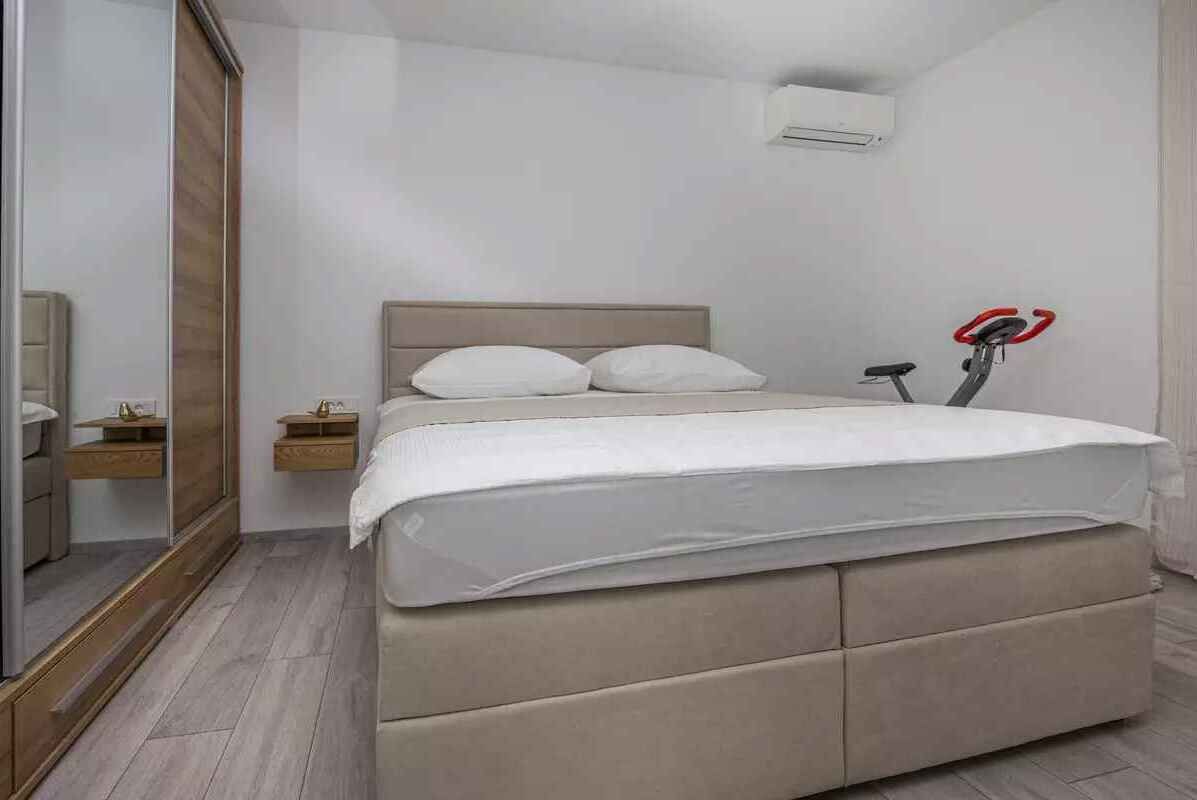 Een slaapkamer met een bed, nachtkastje, spiegel en een wandairconditioner.