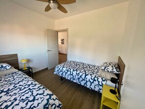 A bedroom with two beds, a ceiling fan, and a door leading to another room.