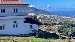A white building with a red-tiled roof, a balcony, and a view of a coastal town and mountains. - Sea View Apt4 Finca TenDays Orotava with Sea View, Wi-Fi and Air Conditioning (La Orotava)