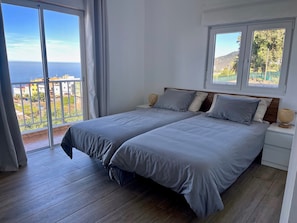 A bedroom with two beds, a balcony, and a view of the sea.
