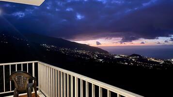 Un balcón con vistas a una ciudad al atardecer, una silla y una barandilla.