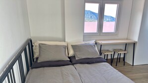 A single bed with a metal frame, a desk with two chairs, and a window with a mountain view.