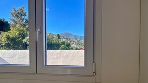 A room with a window overlooking a mountain and greenery.