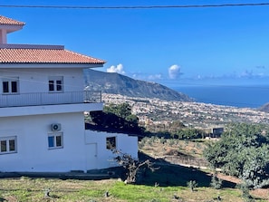 Un bâtiment blanc avec un toit recouvert de tuiles rouges, un balcon et une vue sur une ville côtière et des montagnes.