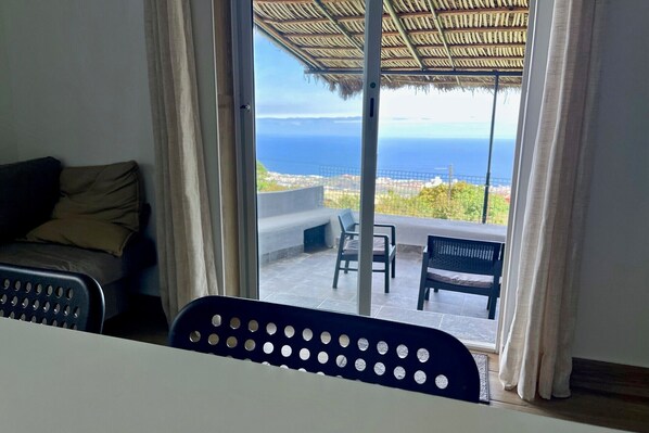A room with a view of the sea, a sofa, a dining table, and a chair.