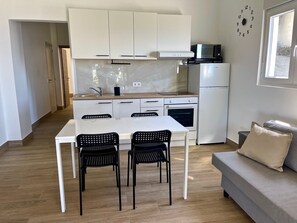 Une cuisine moderne avec des meubles blancs, un four à micro-ondes et un four traditionnel. On y trouve une table à manger avec deux chaises.