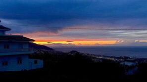 A coastal cityscape at sunset with a prominent building on the left and a view of the ocean.