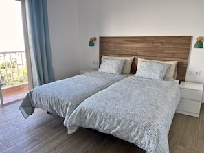 Cama doble con ropa de cama estampada, cabecera de madera, mesitas de noche y vistas al exterior a través de una ventana.