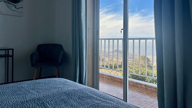 A room with a bed, a chair, and a large sliding glass door leading to a balcony with a view. - Sea View Apt3 Finca TenDays Orotava with Wi-Fi and Air Conditioning (La Orotava)