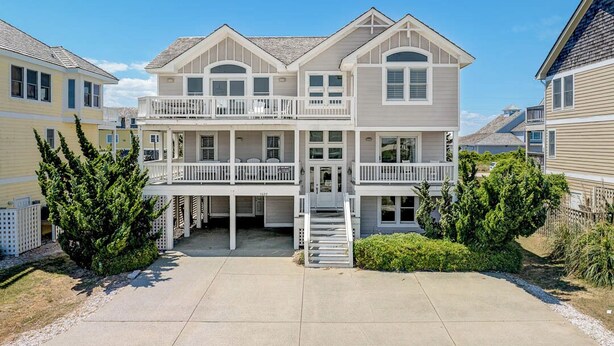 Een twee verdiepingen tellend strandhuis met balkon, een overdekte veranda en een oprit.