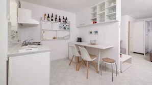 Una cocina moderna con armarios blancos, una estufa integrada y una zona de comedor con dos sillas y una pequeña mesa.