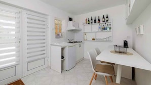 Una cocina compacta con comedor, muebles blancos y una estantería para vinos en la pared.