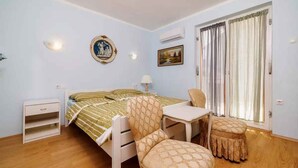 A bedroom with a bed, a desk, a chair, a nightstand, and a window with curtains.