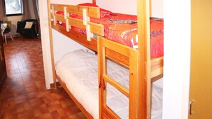 A bunk bed room with a wooden headboard, a lower bunk with a white mattress, and a top bunk with a red patterned mattress. - STUDIO  N° 110 LES FLOCONS (LES ORRES 1650)