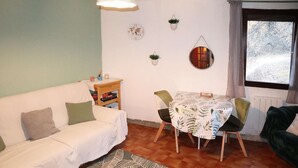 A cozy living room with a white sofa, a dining table with chairs, a small bookshelf, and a window with a view of trees. - STUDIO  N° 110 LES FLOCONS (LES ORRES 1650)