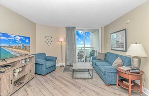 A living room with a TV, two sofas, a coffee table, a lamp, and a balcony with a view.