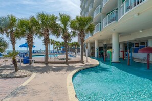 A pool area with palm trees, lounge chairs, and a building with balconies.