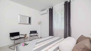 Habitación de hotel con cama, dos sillas, una mesita con una planta, un espejo y un equipo de aire acondicionado.