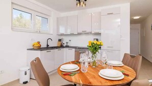 Una cocina moderna con armarios blancos, una mesa de comedor dispuesta con platos y vasos, y un florero con flores.