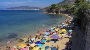 Ein überfüllter Strand mit zahlreichen bunten Sonnenschirmen und Menschen, die das Wasser genießen.